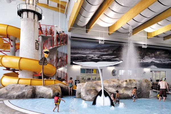 The Oregon-themed aquatics complex is a focal point for the facility. Play features for all ages include a water slide that wraps around a scaled-down replica of the Yaquina Head lighthouse, north of Newport, Ore. The slide plunge pool is surrounded by rock theming and includes a blowhole modeled after a natural feature at Depoe Bay. The blowhole is activated as bathers plunge into the splash zone at the bottom of the slide. Other amenities are floor geysers, interactive spray features, a vortex, and a lazy river that winds through a forest of artificial coniferous trees and doubles as a resistance channel for exercise, therapy and rehabilitation.