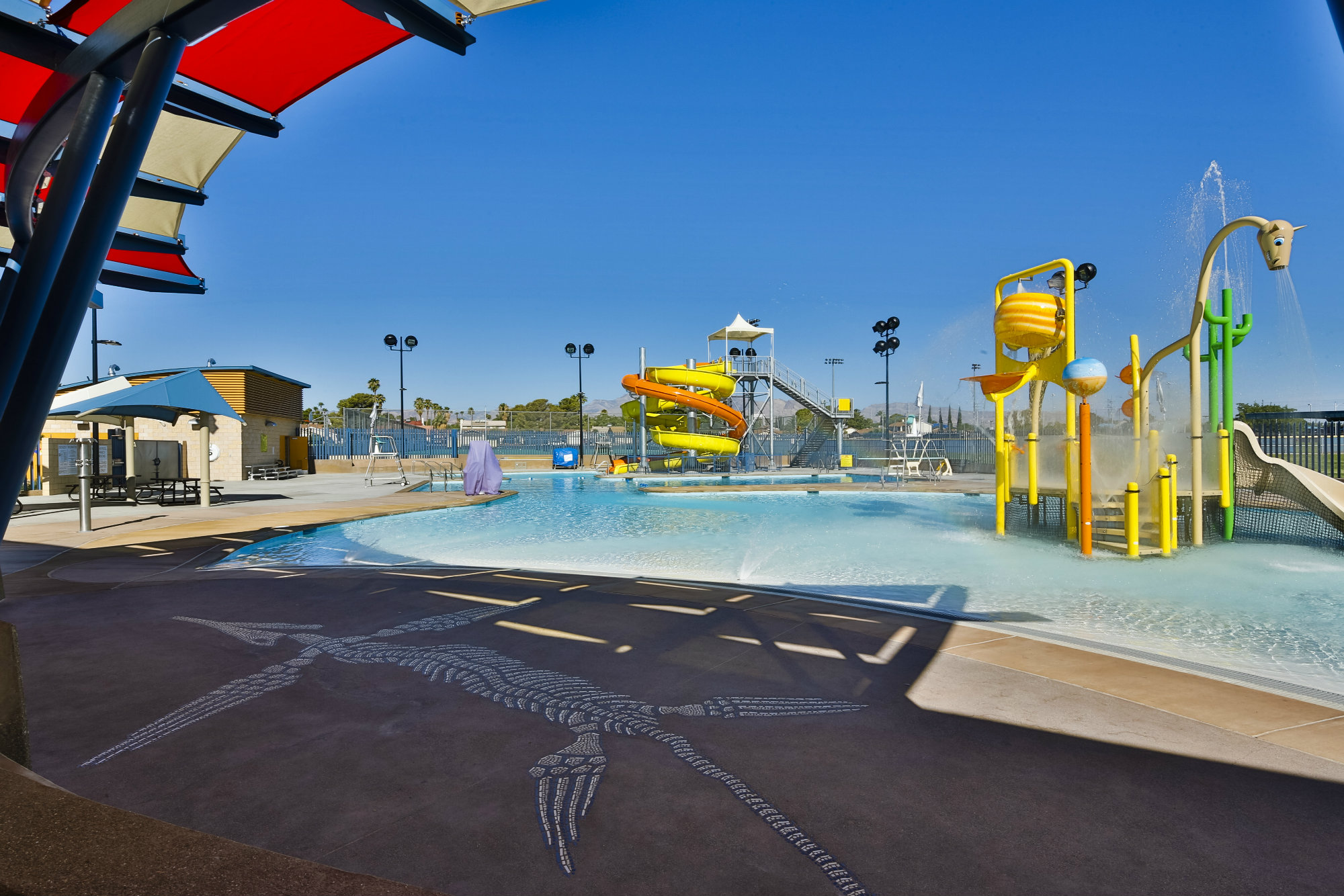 Going way back: Theming recognizes Nevada’s prehistorical geological history. A mosaic set in the recreational pool’s zero-depth entry depicts a fossil, and similar forms were embedded in the concrete decking near the entry-area waterplay feature. The theme was repeated in the foundation and retaining wall for the locker rooms. The locker-room door resembles a icthysoras skeleton. The recreational pool gradually slopes to a 2-1/2 foot maximum depth before connecting with the lap pool. The play structure includes a small open slide, water spray elements and a tipping bucket.t