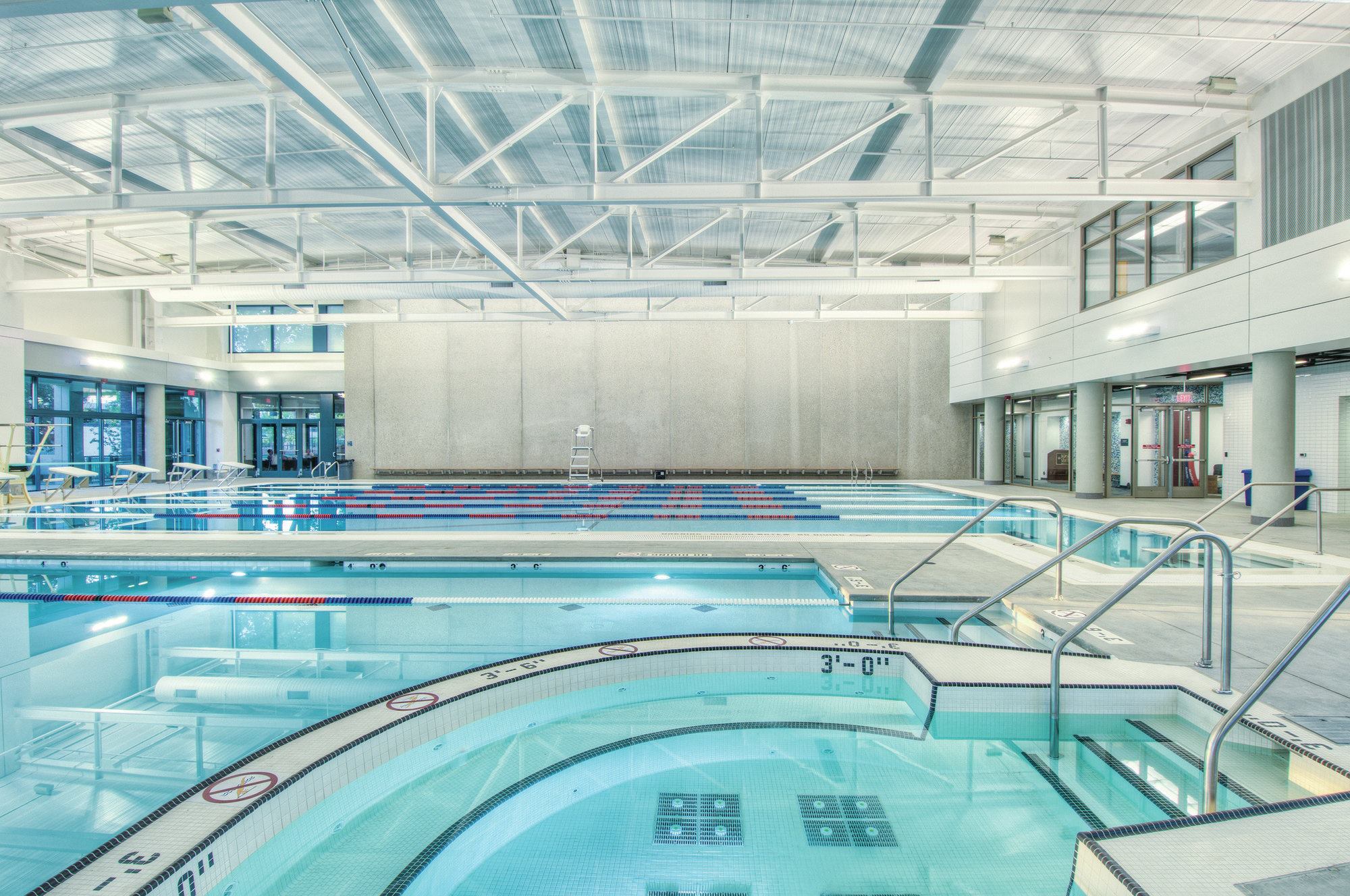 The facility includes a six-lane competition/lap pool measuring 25 yards by 45 feet, with a deck-level gutter system and a current jet system for swimming or kayak training. The facility also is configured to accommodate an aquatic climbing wall in the deep end. The 1,800-square-foot recreational pool features bench seating, volleyball and basketball play area, and is attached to a 120-square-foot, 12-person freeform spa. An in-deck lane-line storage compartment optimizes usable deck space. One of the high white walls is designed to function as a giant movie screen for “dive-in movie” programming.