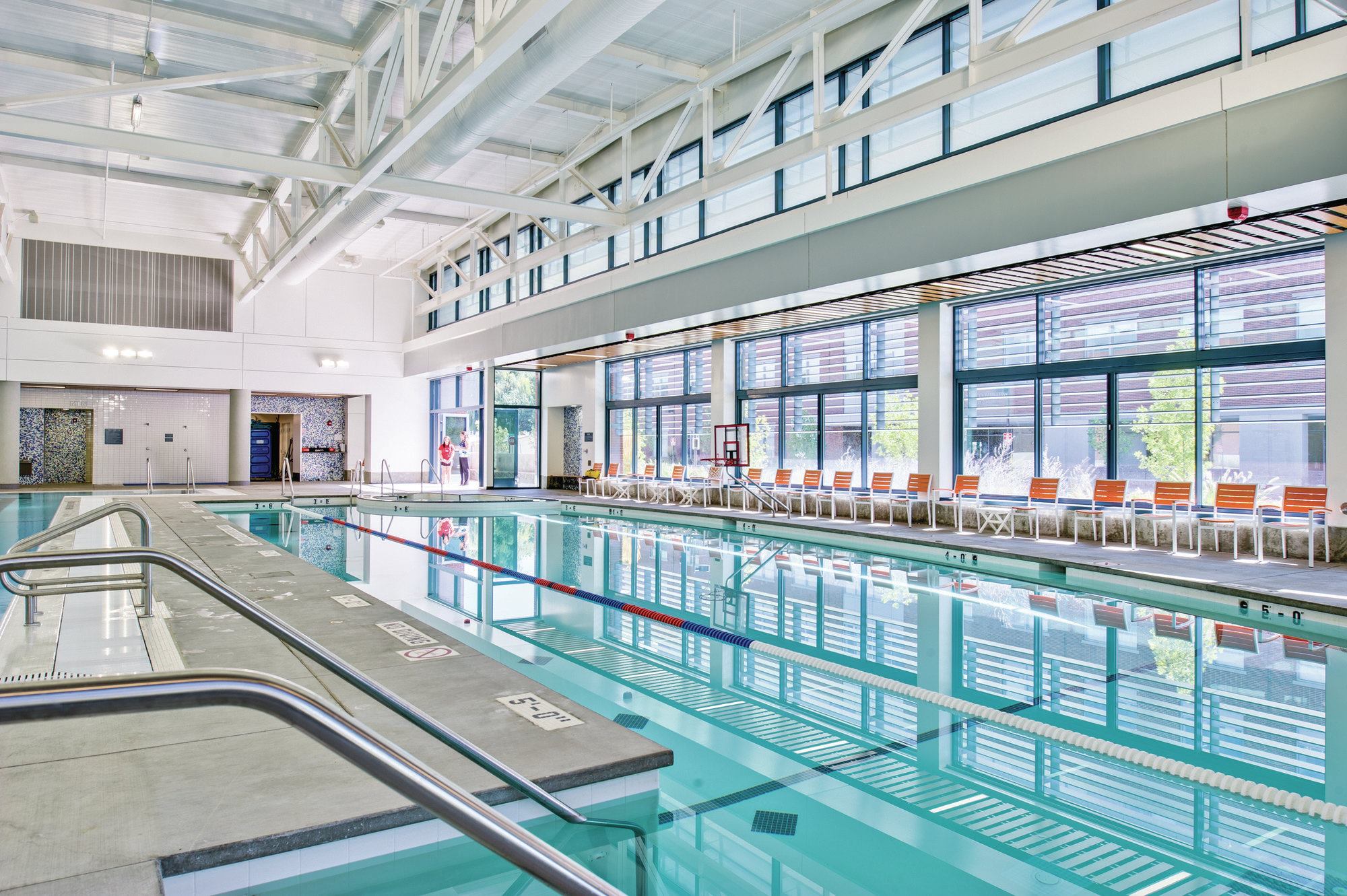Keeping in mind that Boise enjoys sun more than 200 days per year, the design team created the nearly 18,000-square-foot facility to take advantage of as much natural light as possible and connect with the environs. Large, operable windows on three sides provide a direct visual connection to the outdoors. A continuous skylight creates shadow patterns, and clerestory windows bring in reflected daylight, which balances the space. In warm weather, a large sliding door can open and create a connection to the outdoor terraces. The windows and skylight also provide ventilation when weather allows, thereby adding to energy efficiency. To that end, the team also had solar panels installed on the roof to aid with the pool heating and HVAC system. Blue mosaic tiles on the vertical surfaces echo waterfeatures, while the white of the ceilings, structure and high walls put the focus where it belongs — on the blue water.