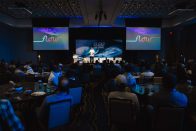 A speaker presents at the SURF PARK SUMMIT to a seated audience in a conference room, featuring a backdrop with colorful "flow" text and ocean imagery.